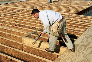 Worker gluing plywood flooring to I-joist